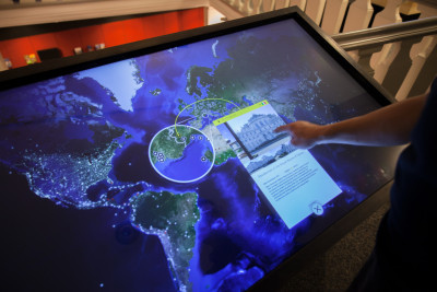 Person interacting with touchscreen; touchscreen shows world map and text