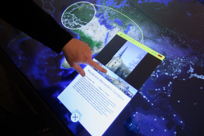 Hand interacting with touchscreen; touchscreen shows world map and text